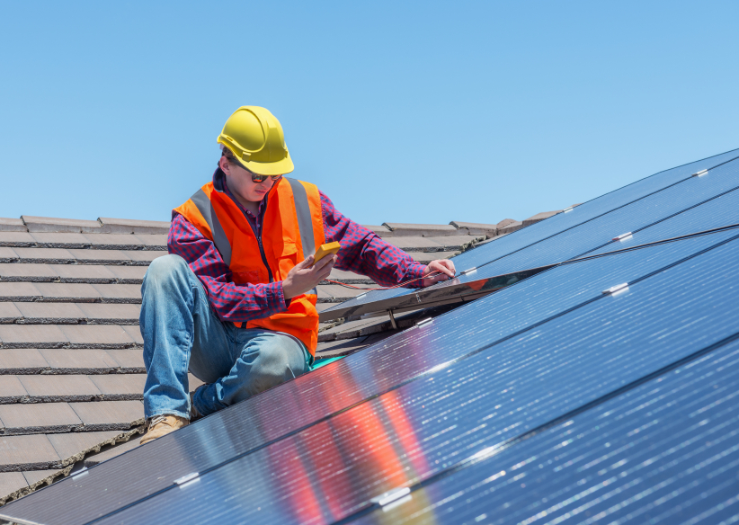 Construction worker inspecting solar panels on a tiled roof.
